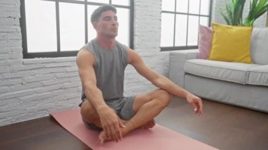 Genç bir adam yoga yapıyor. Parlak, modern bir apartman dairesinde..