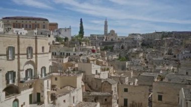 Basilicata, İtalya 'daki materyalin panoramik görüntüsü, tarihi taş binalar, manzaralı çatılar, ve parlak mavi gökyüzünün altındaki uzak bir kilise.