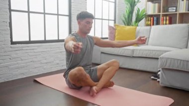 Şık bir oturma odasında pembe yoga minderinin üzerinde esneyen, dinginlik ve huzur saçan, kaslı, genç bir İspanyol..