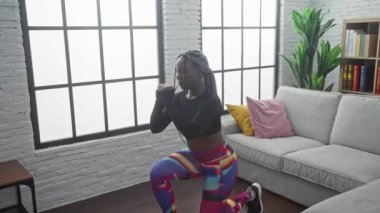 Oturma odasında kanepe ve pencereyle egzersiz yapan Afrikalı kadın.