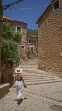 Taş basamaklarda yürüyen bir kadın Mallorca, İspanya 'da, açık mavi gökyüzünün altında, tarihi binalar ve canlı yeşilliklerle çevrili tuhaf bir köyde