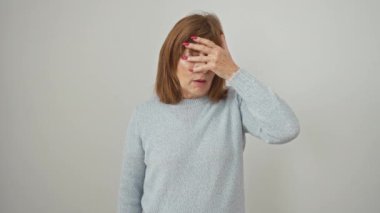 Orta yaşlı İspanyol kadın ayakta dikilip şok olmuş bir şekilde yüzünü ve gözlerini kapayarak utanmış bir ifadeyle parmaklarından bakıyor. izole edilmiş beyaz arkaplan