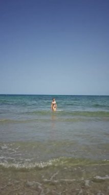Bikinili kadın açık mavi okyanusta güneşli bir gökyüzünün altında güzel bir sahilde duruyor.