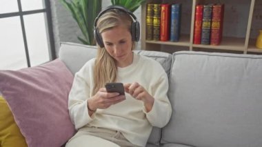 Rahatlamış bir kadın, kulaklıkla müzik dinlerken kapalı bir koltukta akıllı telefon kullanır..