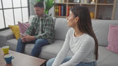 İspanyol kadın ve erkek birlikte oturma odasında, erkek cep telefonu kullanırken gerilim gösteriyor ve kadını görmezden geliyor..