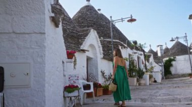 Güneşli bir günde, tarihi Alberobello, Puglia, İtalya ve Avrupa 'da büyüleyici bir caddedeki ilginç trulli evlerini keşfeden yeşil elbiseli genç İspanyol kadın..