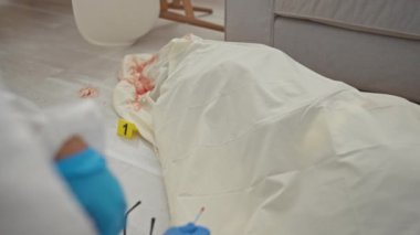 Adli tıp uzmanı. Modern bir oturma odasındaki suç mahallinde kan örneklerini inceliyor.