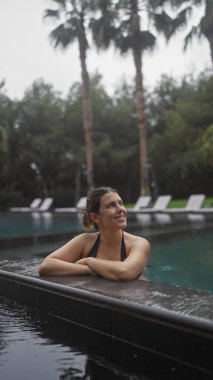 Gülümseyen genç kadın tropik palmiyelerle çevrili lüks bir bali tatil köyünde dinleniyor..