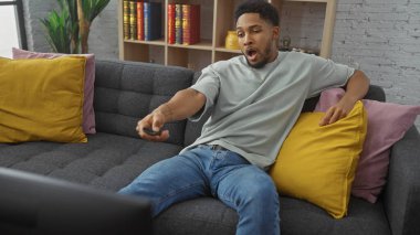 Afro-Amerikalı bir adam uzaktan kumandayla esniyor, kanepede uzanıyor..