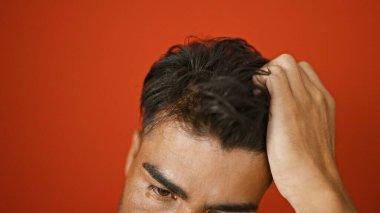 Sakallı genç bir İspanyol adam, erkeklik ve çekicilik saçan canlı kırmızı bir duvara karşı düşünceli bir şekilde poz verir..