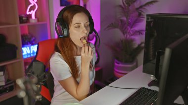 Kulaklığı olan odaklanmış genç bir kadın, gece hareketli bir oyun odasında atıştırmanın tadını çıkarıyor..