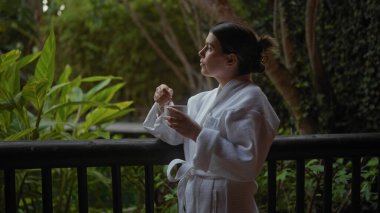 Beyaz cüppeli sakin bir kadın, bali tatil köyünün terasında bir fincan kahveyle sakin bir sabahın tadını çıkarıyor..