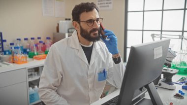 Laboratuvar önlüklü sakallı bir adam laboratuarda bilimsel ekipmanlarla konuşuyor..