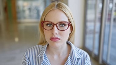 Kırmızı gözlüklü genç sarışın kadın, ince çizgili bir gömlek içinde, şehir sokaklarındaki zarafeti somutlaştırıyor..