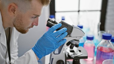 Modern bir laboratuvar ortamında mikroskop ayarlayan yakışıklı beyaz adam.