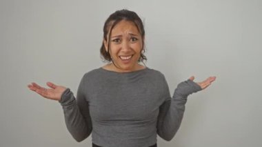 Beyaz arka plan üzerinde duran şaşkın genç İspanyol kadın, yüzündeki şüphe ifadesinden bihaber.