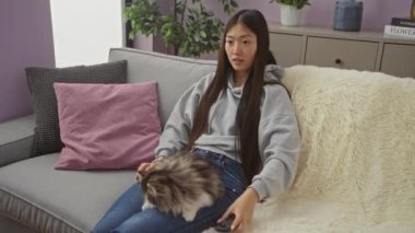 Genç Asyalı kadın rahat bir oturma odasında kanepede kedisiyle otururken mutlu bir şekilde kutluyor..