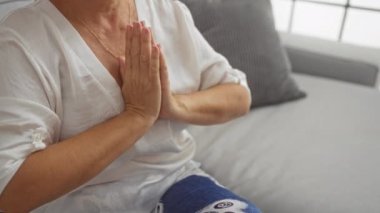 Yaşlı bir kadın oturma odasındaki rahat bir kanepede ellerini birbirine bastırıp, huzur ve sükunet içinde meditasyon yapıyor..