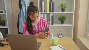 Ofisteki akıllı telefonu kullanan İspanyol kadın laptopu, fincanı ve bitkiyi masaya koydu.