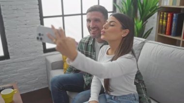 Mutlu bir çift şık evlerinin oturma odasındaki kanepede selfie çeker..