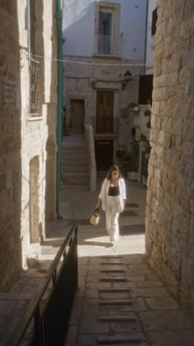 Genç İspanyol bir kadın polignano 'nun büyüleyici taş caddelerinde yürüyor Puglia, İtalya' da bir kısrak güneş ışığıyla yıkanmış ve tarihi mimariyle çevrili..