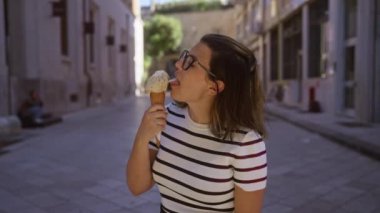 Puglia, İtalya 'da güneşli bir günde çizgili gömlekli genç bir İspanyol kadın dondurma külahının tadını çıkarıyor..