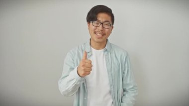 Gözlüklü, neşeli, genç Çinli bir adam geniş bir gülümseme takınıyor ve harika bir işaret veriyor. İzole edilmiş beyaz bir arkaplan karşısında sırdaş, neşe ve pozitif titreşimler yayıyor..