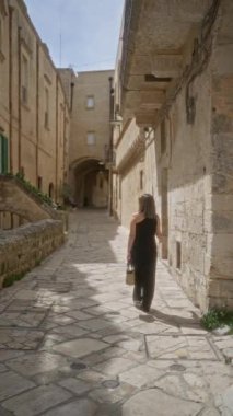 Siyah elbiseli genç bir kadın Materya, Basilicata, İtalya 'nın antik taş caddelerinde yürüyor. Eski şehrin tarihi mimarisini ve sakin atmosferini vurguluyor..