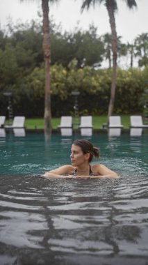 Güzel, genç bir İspanyol kadın lüks bir bali tatil köyünde serin bir açık havuzda yüzüyor..