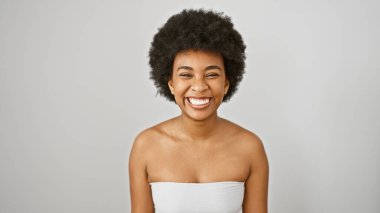 Kıvırcık saçlı, gülümseyen Afro-Amerikan bir kadın beyaz bir arka plana karşı poz veriyor..
