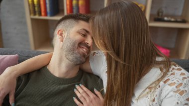 Gülümseyen bir adam ve bir kadın kitaplarla süslenmiş sıcak bir oturma odasında kucaklaşıyorlar.