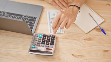 Bilgisayarın yanında hesap makinesi kullanan bir adamın eline yakın çekim ve ofis ortamındaki ahşap bir masada dolarlarımız..