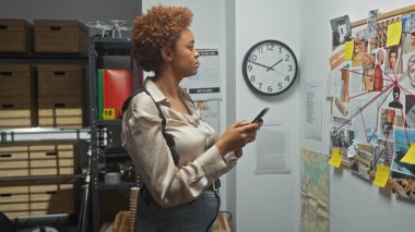 An african american woman analyzes evidence in a police station with a detective board in the background. clipart