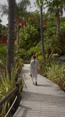 Bali tatil köyü bahçesinde gezen genç bir kadın gevşeme ve tropikal zarafeti temsil ediyor..