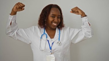 Beyaz önlük ve steteskopla güvenle gülümseyen genç Afrikalı Amerikalı kadın doktor, izole edilmiş beyaz arka planda poz veriyor.