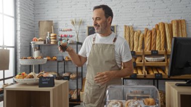 Taze ekmek ve pastalarla çevrili bir fırında çalışan orta yaşlı bir adam, müşterilere sıcak kapalı dükkânda maşa ile servis yaparken gülümsüyor..