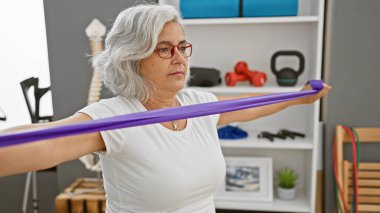 Olgun bir kadın fizik tedavi kliniğinde direniş bandıyla egzersiz yapıyor..