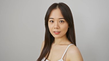 Düz beyaz bir arkaplan üzerinde duran, sakin bir ifadeyle Asyalı genç bir kadının portresi..