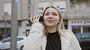 Genç sarışın kadın şehrin hareketli caddesinde akıllı telefon kullanıyor.