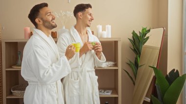 Erkekler spa sağlık odasında rahatlatıcı bir anın tadını çıkarıyorlar. Cübbe giyiyorlar ve ellerinde fincanlar, rahatlatıcı dekorlar ve mumlarla.