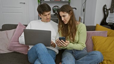 Konforlu oturma odalarında teknolojiyle meşgul bir çift akıllı telefon kullanan bir kadını ve dizüstü bilgisayarla çalışan bir adamı sergiliyor..