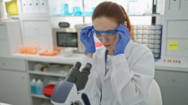 Kafkasyalı genç bir kadın bilim adamı laboratuvar ortamında mikroskop kullanarak örnekleri analiz ediyor..