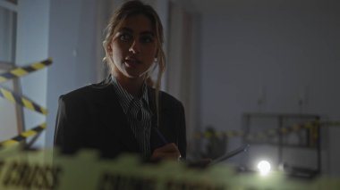 Düşünceli genç bir kadın loş bir suç mahallini araştırıyor, ön plandaki uyarı bandı yer çekimini işaret ediyor..