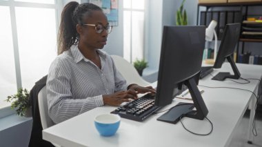 Ofiste çalışan bir kadın, elinde bilgisayarla iç mekanda oturuyor ve Afro-Amerikan bir kadının daktilo yazıp gözlük taktığını anlatıyor.