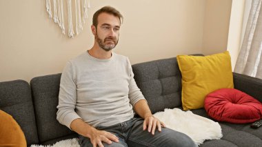 Rahat orta yaşlı bir adamın portresi. Sakallı, rahat bir oturma odasında kanepede oturuyor..