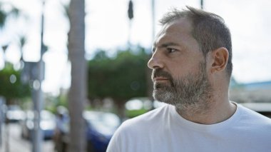 Şehir dışında beyaz saçlı, olgun İspanyol bir adam, düşünceli bir şekilde şehir sokağına bakıyor..