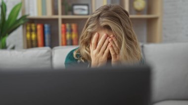 Sarışın kadın elleri ile yüzünü kapatır. Stres ya da baş ağrısı olur.