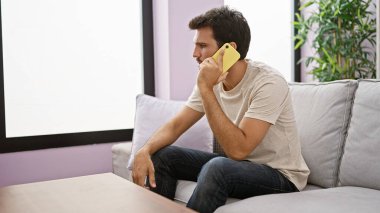 İspanyol bir adam modern bir oturma odasında telefonla konuşuyor ve iç mekan düzenine gelişigüzel bir iletişim hissi katıyor..