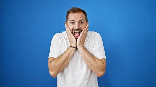 stock image A surprised hispanic mature man with grey hair, outdoors against a blue wall, portraying genuine human emotion.