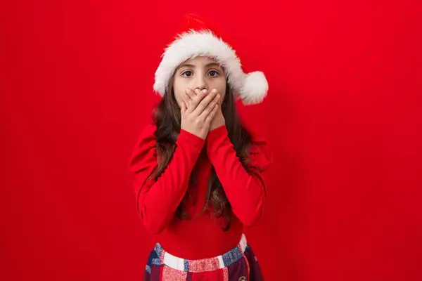 stock image Shocked hispanic girl, adorable and worried, covers mouth at a christmas secret blunder. hands over mouth, astonished expression on red isolated background.